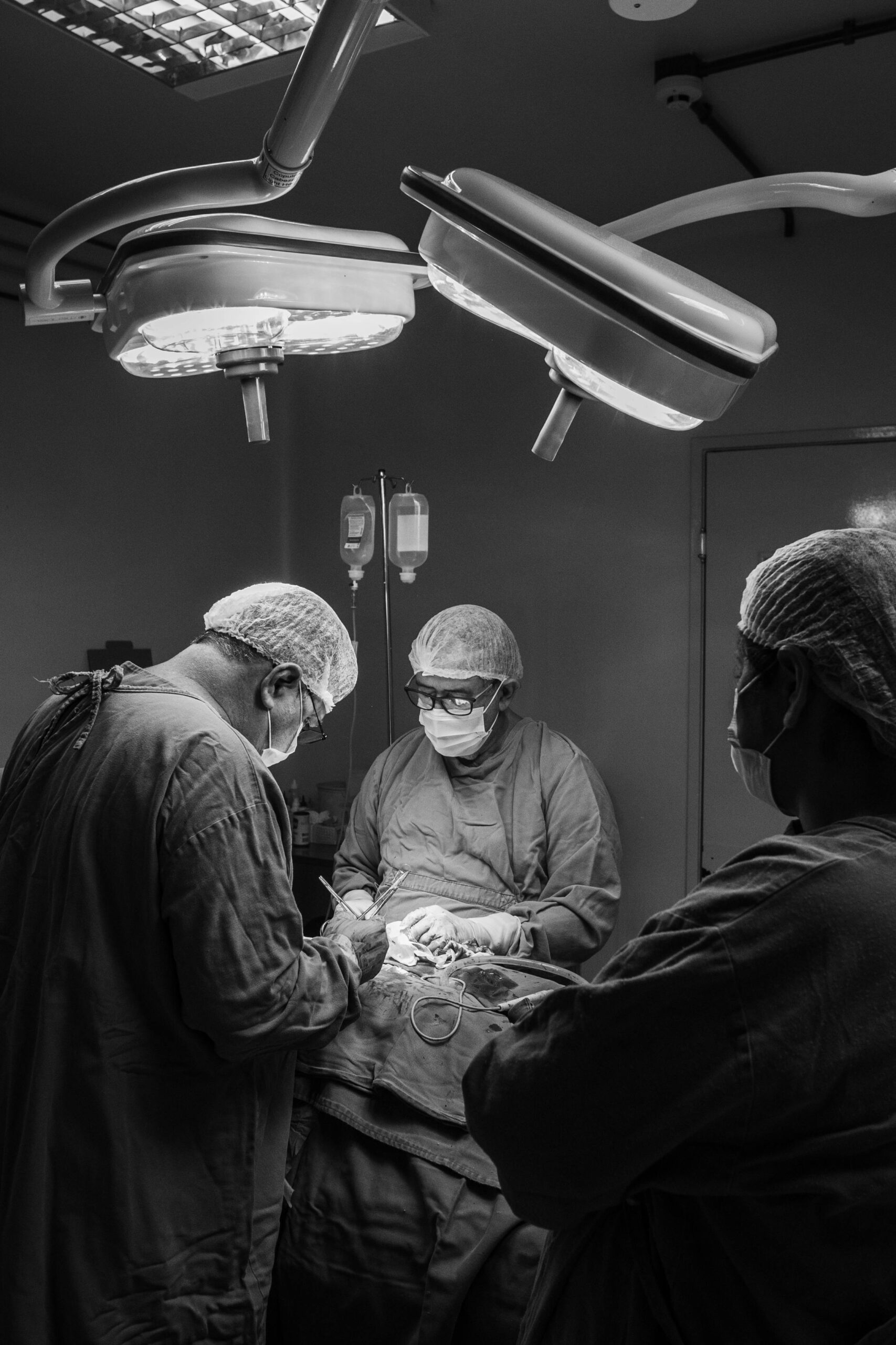 Surgeons performing surgery in a hospital operating room, captured in black and white.