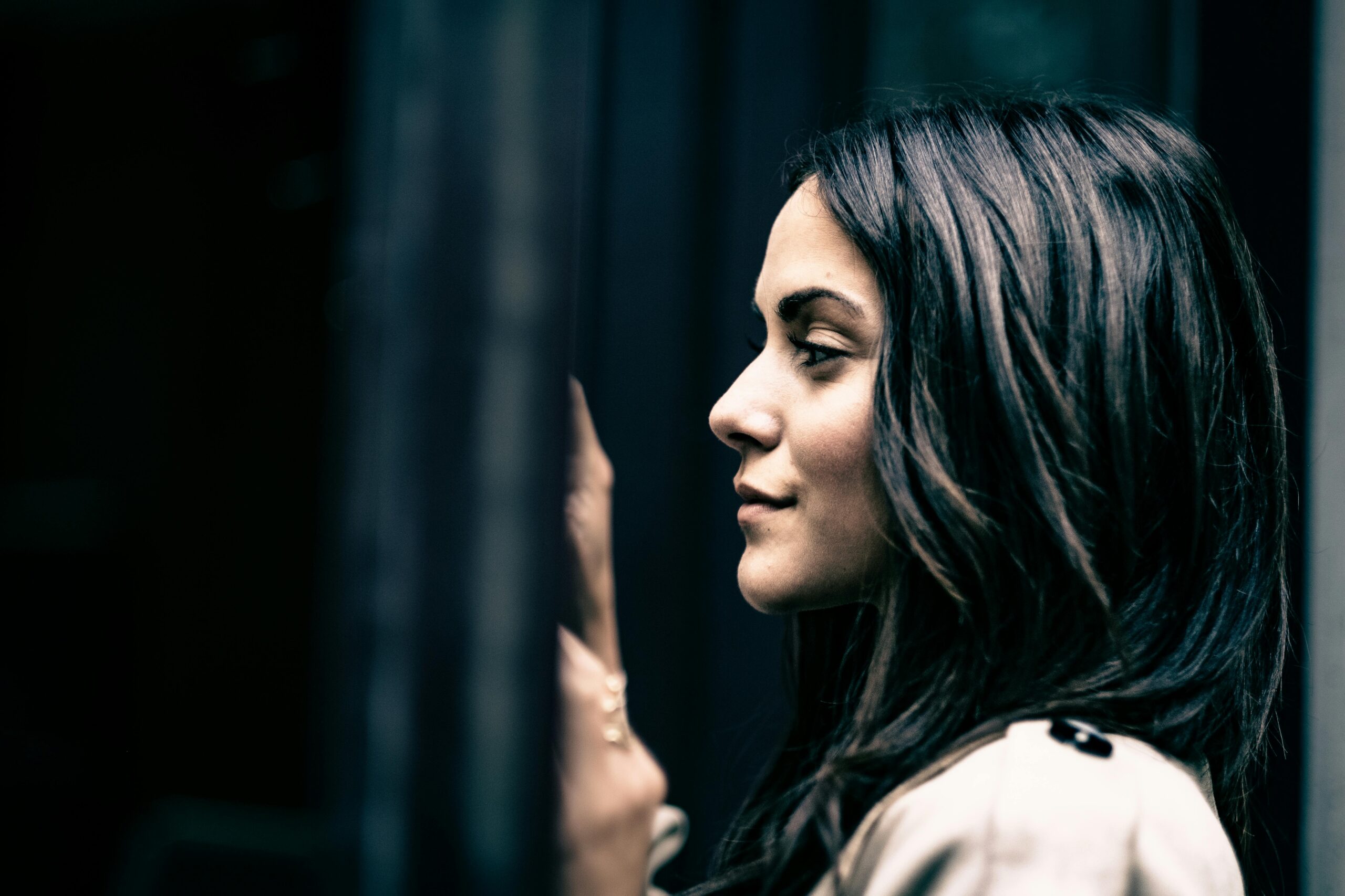 Artistic side profile of a woman with black hair leaning against a wall in low light.