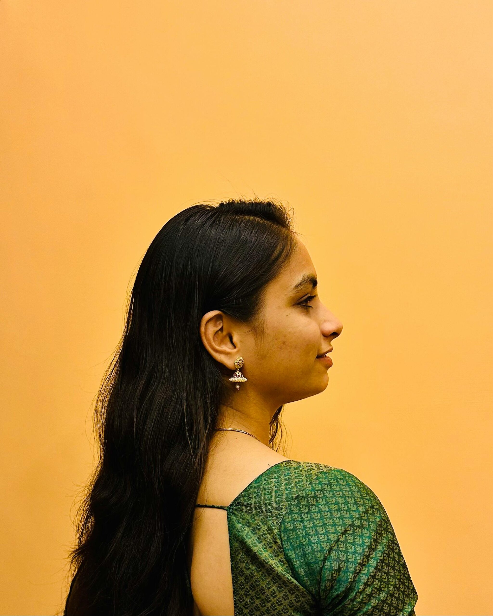 Elegant side profile of a South Asian woman in a green sari against a warm background.